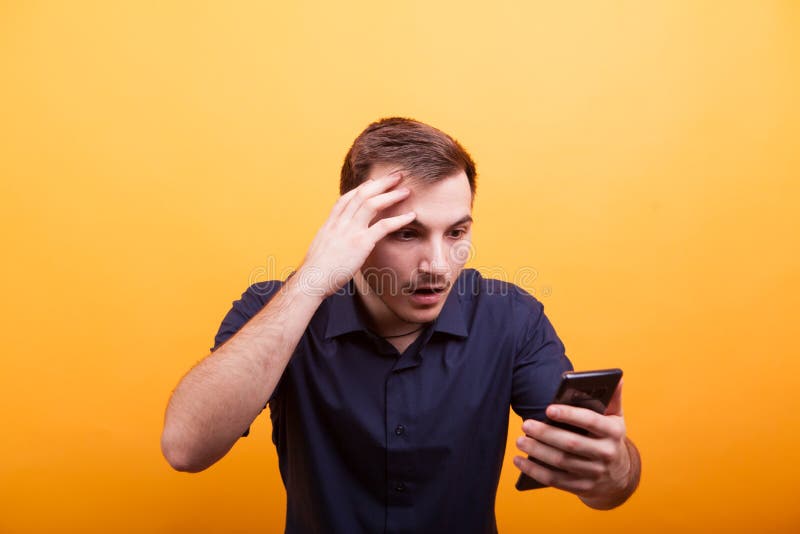 Hombre joven que parece chocado en su teléfono en fondo amarillo imágenes de archivo libres de regalías Hombre joven que parece chocado en su teléfono en fondo amarillo imágenes de archivo libres de regalías