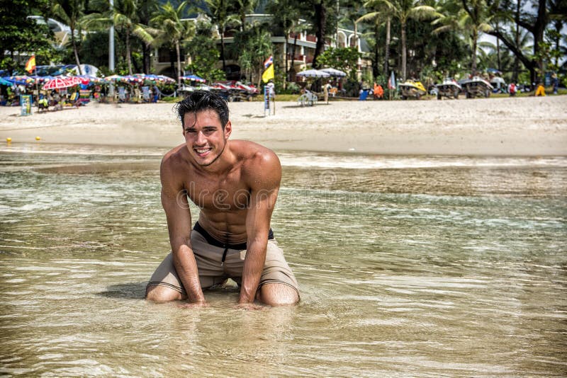 Hombre joven que se arrodilla en una playa tropical imágenes de archivo libres de regalías Hombre joven que se arrodilla en una playa tropical imágenes de archivo libres de regalías
