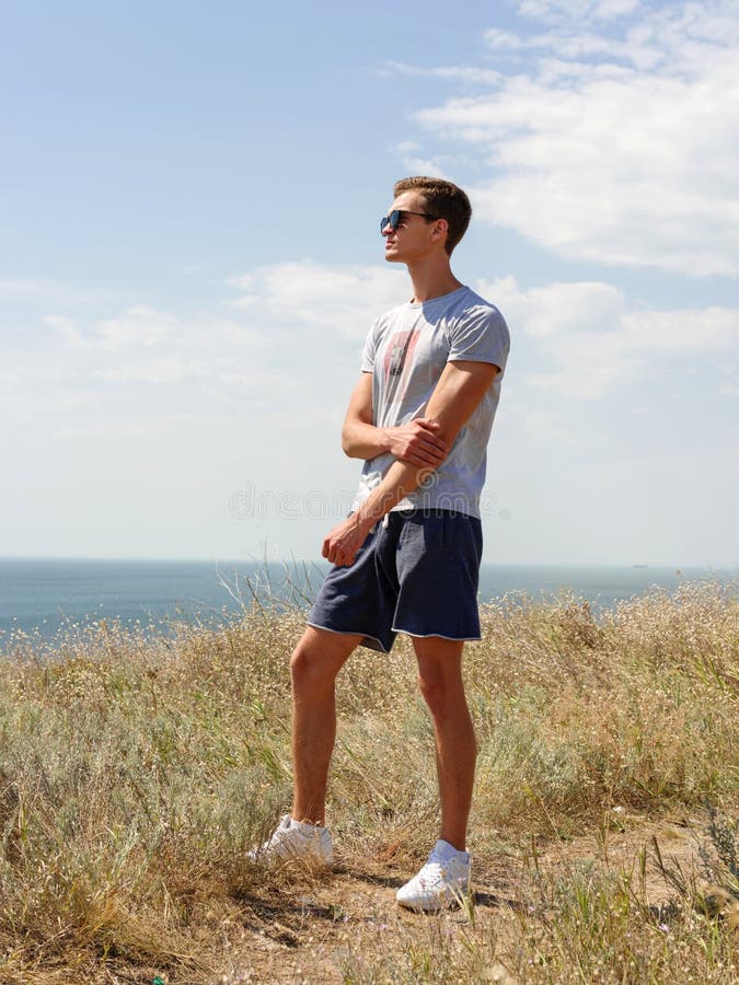 Hombre joven que se coloca y que presenta encima del acantilado en montañas del verano en la puesta del sol y que disfruta de la imagen de archivo libre de regalías Hombre joven que se coloca y que presenta encima del acantilado en montañas del verano en la puesta del sol y que disfruta de la imagen de archivo libre de regalías