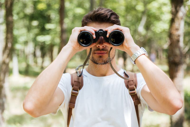 Hombre joven serio con la mochila usando los prismáticos en bosque fotografía de archivo Hombre joven serio con la mochila usando los prismáticos en bosque fotografía de archivo