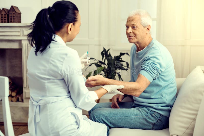Hombre jubilado alegre que mira al trabajador médico que lo vacuna imagen de archivo Hombre jubilado alegre que mira al trabajador médico que lo vacuna imagen de archivo
