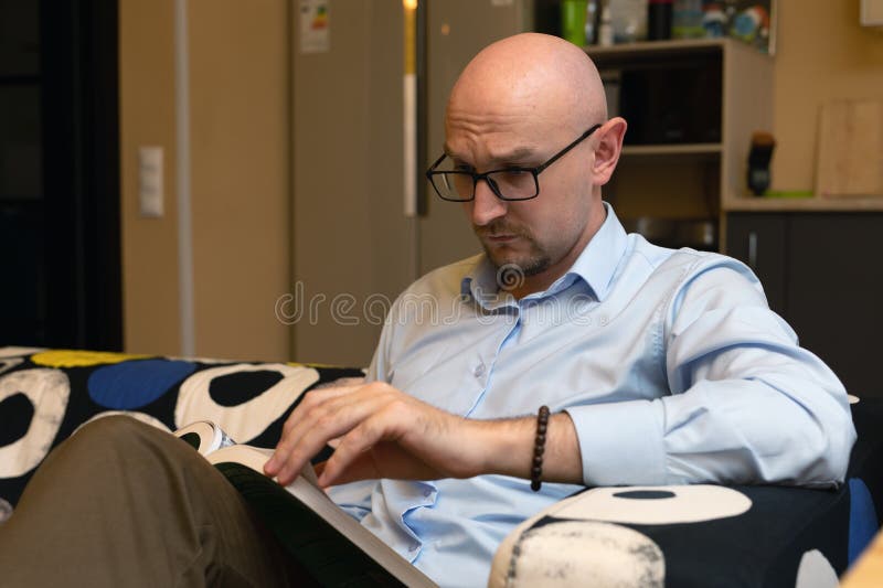 Hombre leyendo libro en casa sentado en un sofá en una sala de estar moderna. pasatiempo plasmático fotografía de archivo