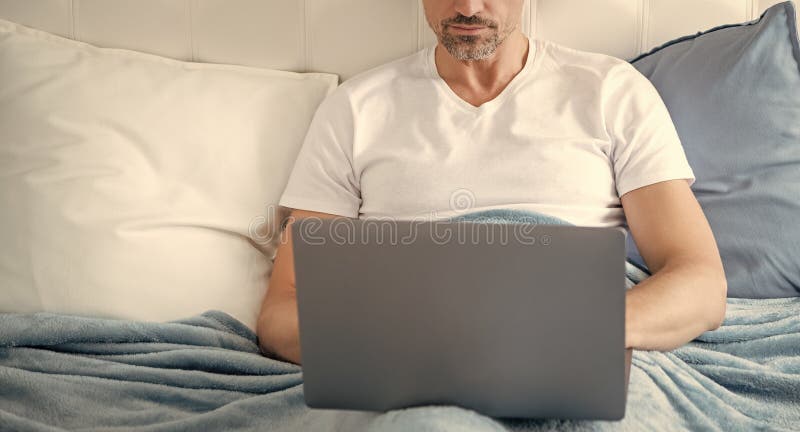 Hombre maduro trabajando en una laptop en la cama. negocios en línea foto de archivo