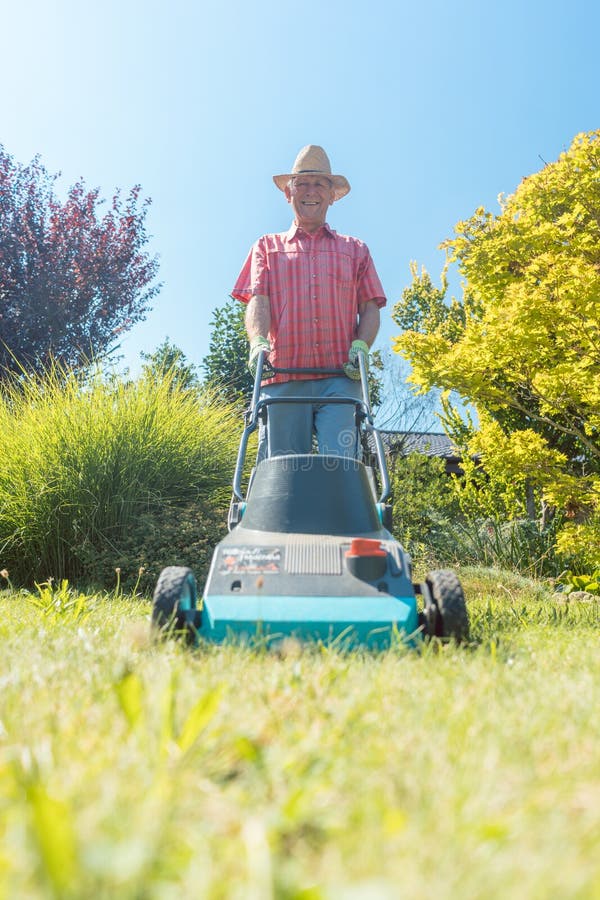 Hombre mayor activo que sonríe mientras que usa una cortadora de la hierba en el jardín fotografía de archivo libre de regalías Hombre mayor activo que sonríe mientras que usa una cortadora de la hierba en el jardín fotografía de archivo libre de regalías