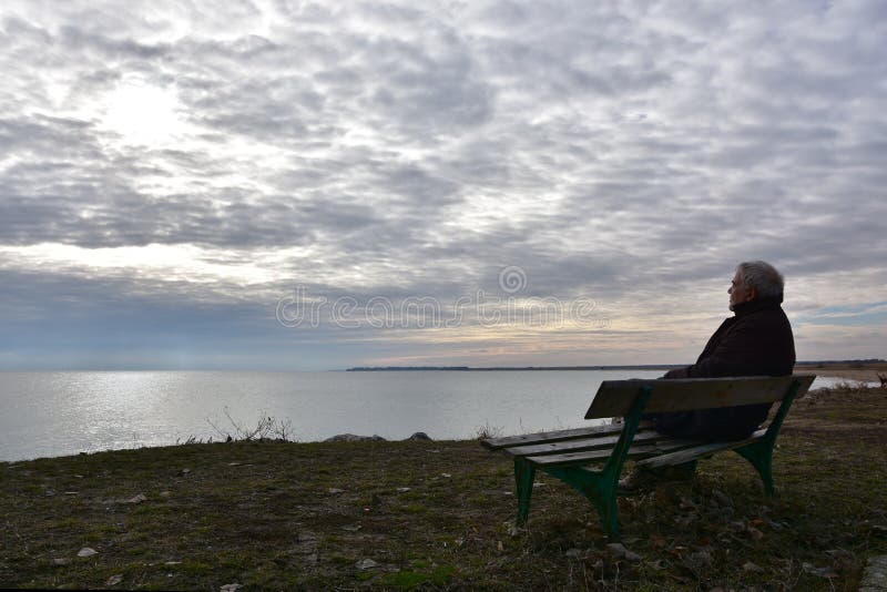 Hombre mayor en una banca viendo la temporada de invierno imagenes de archivo Hombre mayor en una banca viendo la temporada de invierno imagenes de archivo