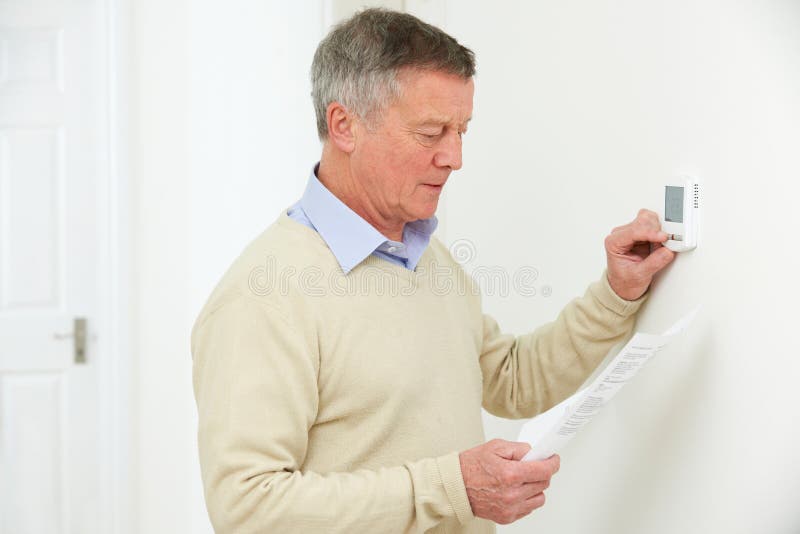 Hombre mayor preocupante con Bill Turning Down Heating Thermostat imagen de archivo libre de regalías Hombre mayor preocupante con Bill Turning Down Heating Thermostat imagen de archivo libre de regalías