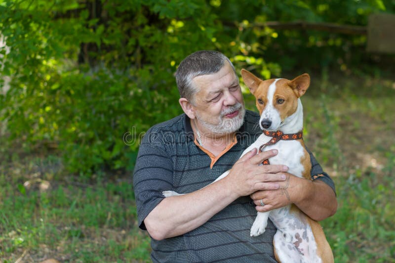 Hombre mayor que habla con su basenji lindo del perro que lo toma en las manos mientras que descansa en parque del verano imagen de archivo libre de regalías Hombre mayor que habla con su basenji lindo del perro que lo toma en las manos mientras que descansa en parque del verano imagen de archivo libre de regalías
