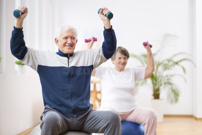 Hombre mayor y mujer que ejercitan en bolas gimnásticas durante la sesión de la fisioterapia en el hospital