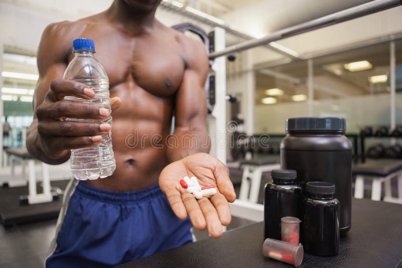 Hombre muscular descamisado que sostiene píldoras de la vitamina imagen de archivo libre de regalías Hombre muscular descamisado que sostiene píldoras de la vitamina imagen de archivo libre de regalías