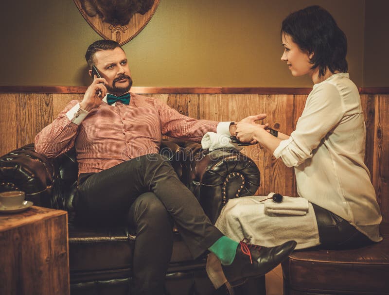 Hombre pasado de moda confiado que habla en el teléfono móvil y que hace la manicura masculina en una peluquería de caballeros imagenes de archivo Hombre pasado de moda confiado que habla en el teléfono móvil y que hace la manicura masculina en una peluquería de caballeros imagenes de archivo