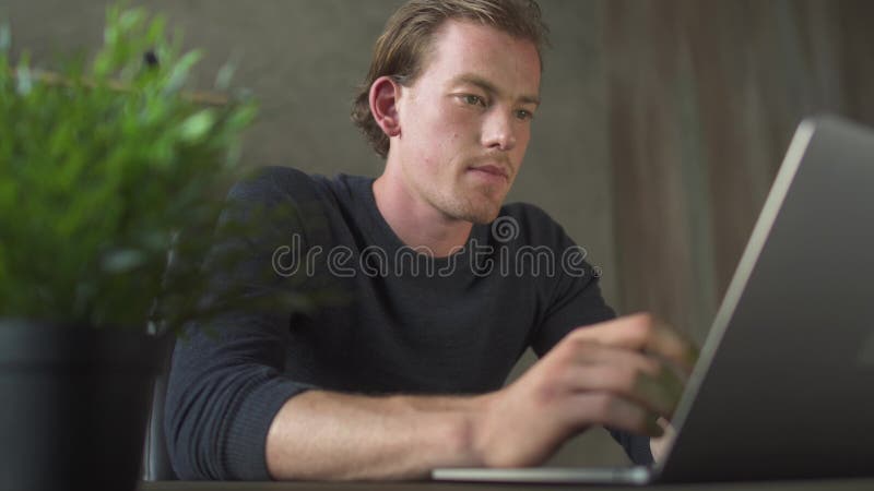 Hombre preocupante rubio joven que se sienta en la tabla de la oficina y que trabaja en el cuaderno Hombre de negocios hermoso qu