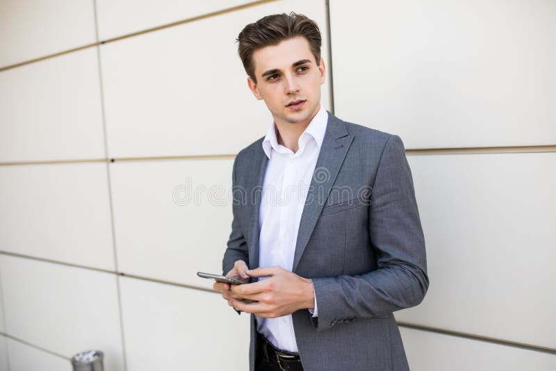 Hombre profesional urbano joven que usa el teléfono elegante en el edificio de oficinas dentro Hombre de negocios que sostiene sm imagenes de archivo Hombre profesional urbano joven que usa el teléfono elegante en el edificio de oficinas dentro Hombre de negocios que sostiene sm imagenes de archivo