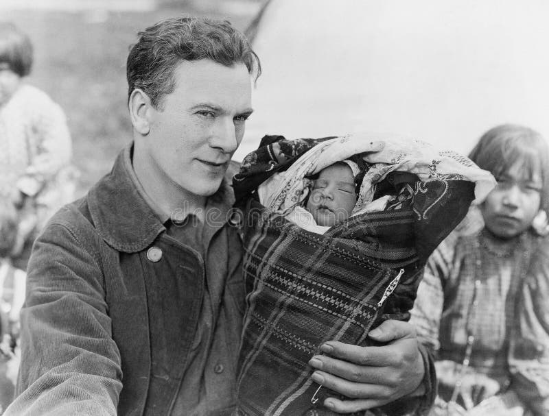 Hombre que detiene al bebé durmiente en papoose (todas las personas representadas no son vivas más largo y ningún estado existe G fotografía de archivo libre de regalías
