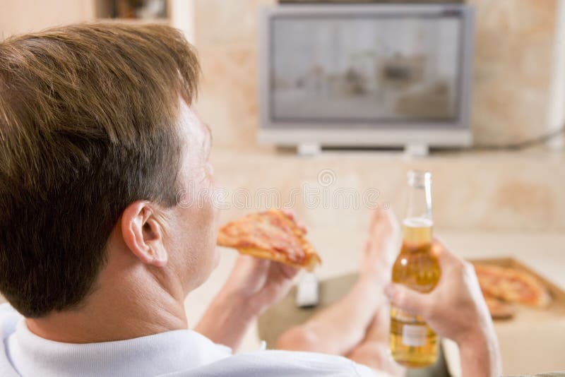Hombre que goza de la cerveza y de la pizza delante de la TV imagen de archivo libre de regalías Hombre que goza de la cerveza y de la pizza delante de la TV imagen de archivo libre de regalías