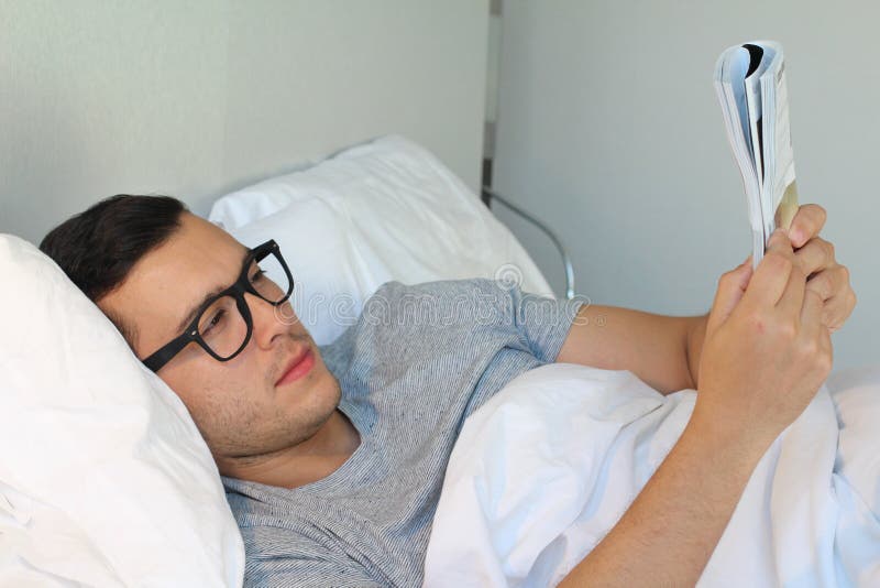 Hombre que lee una revista en cama imágenes de archivo libres de regalías Hombre que lee una revista en cama imágenes de archivo libres de regalías