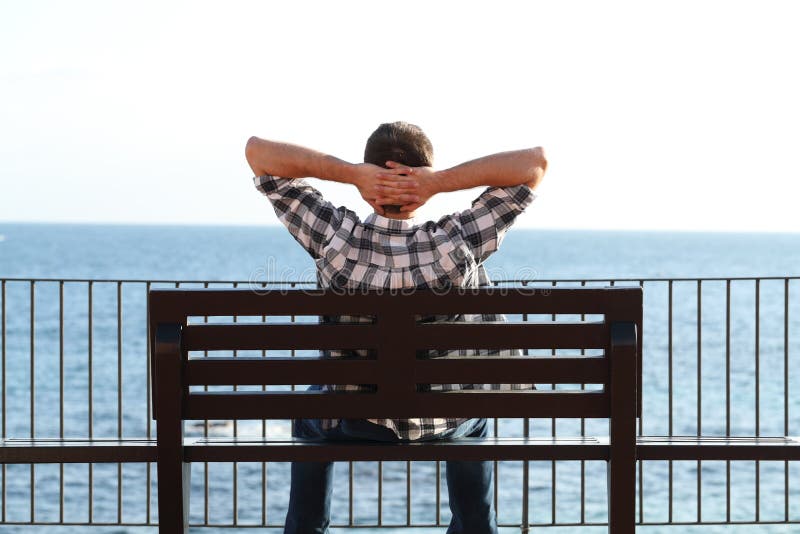 Hombre que se relaja en la playa que se sienta en un banco imagenes de archivo Hombre que se relaja en la playa que se sienta en un banco imagenes de archivo