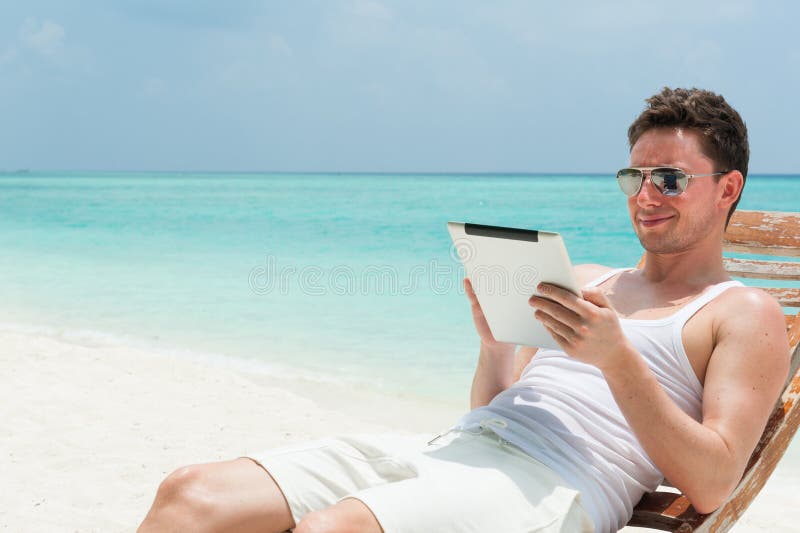 Hombre que se sienta con la tableta en la playa imagenes de archivo Hombre que se sienta con la tableta en la playa imagenes de archivo
