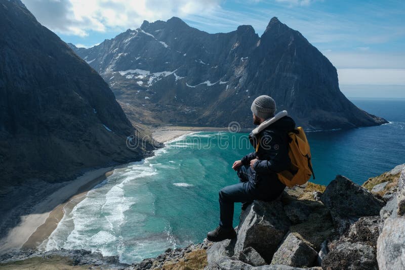 Hombre que se sienta en el borde del acantilado solamente que disfruta de la visión aérea que hace excursionismo vacaciones al ai