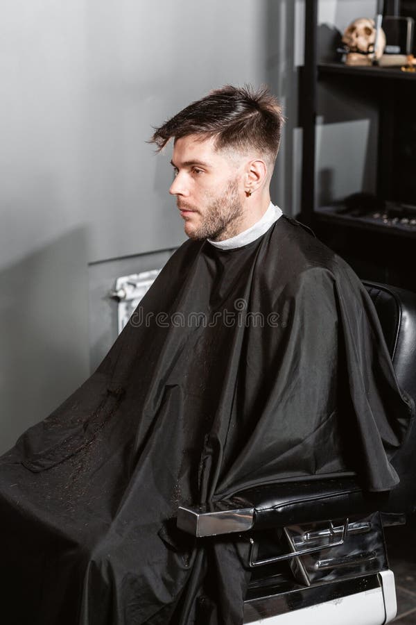 Hombre que se sienta en una silla de peluquero El pelo de los cortes y la barba principales de los hombres en la barber?a, peluqu fotografía de archivo Hombre que se sienta en una silla de peluquero El pelo de los cortes y la barba principales de los hombres en la barber?a, peluqu fotografía de archivo