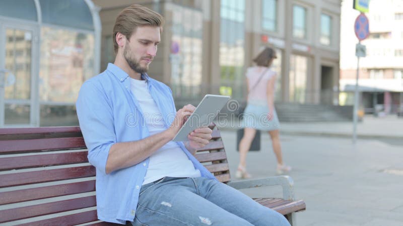 Hombre que usa tableta mientras se sienta al aire libre en el banco imagen de archivo libre de regalías