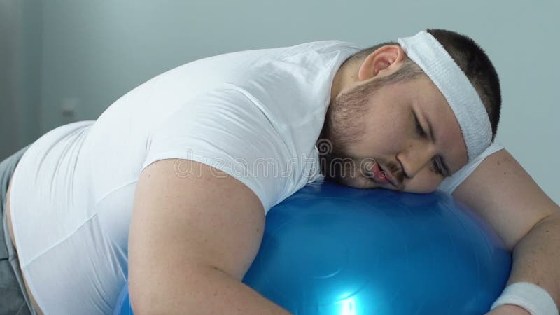 Hombre rechoncho perezoso que se relaja en la bola de la aptitud, falta de motivación del deporte, futilidad almacen de metraje de vídeo