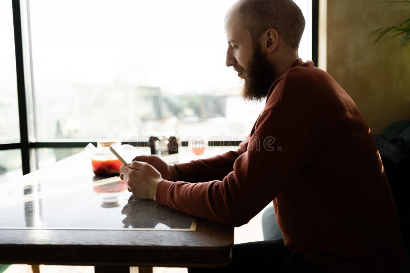 Hombre sentado cerca de la ventana en el café mirando el celular y charlando con sus amigos. foto de archivo