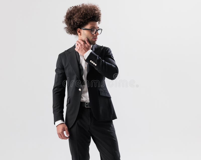 Hombre sexy con pelo rizado y gafas tocando el cuello y mirando hacia un lado imagenes de archivo