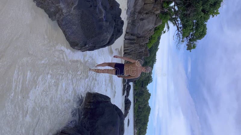 Hombre sin camisa caminando entre rocas a orillas del mar en la isla