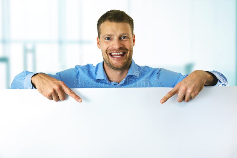 Hombre sonriente apuntando a una pizarra en blanco con espacio para copiar imagen de archivo libre de regalías Hombre sonriente apuntando a una pizarra en blanco con espacio para copiar imagen de archivo libre de regalías