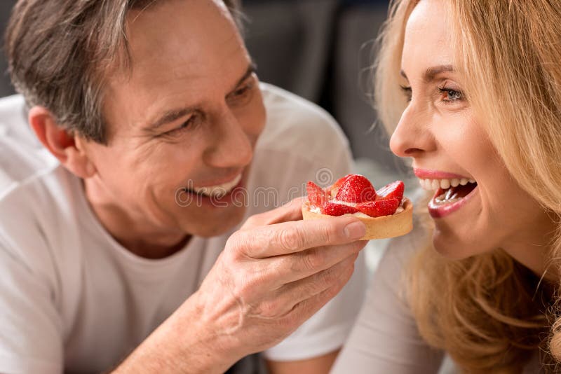 Hombre sonriente que alimenta a la mujer rubia hermosa en la mañana foto de archivo libre de regalías Hombre sonriente que alimenta a la mujer rubia hermosa en la mañana foto de archivo libre de regalías