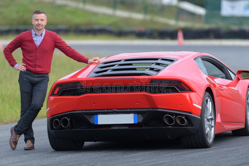 Smiling man posing against red sport car on a circuit. Smiling man posing against red sport car on a circuit