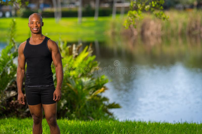 Hombre sonriente que presenta por un lago en el parque foto de archivo libre de regalías