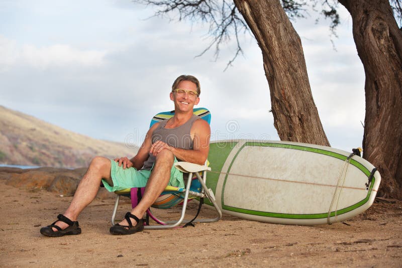Hombre sonriente que se sienta con la tabla hawaiana imágenes de archivo libres de regalías Hombre sonriente que se sienta con la tabla hawaiana imágenes de archivo libres de regalías