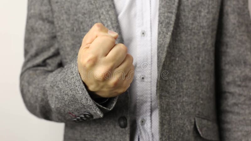 Hombre sólido en chaqueta gris en el fondo blanco que tira el puño hacia arriba. Concepto del gesto de la amenaza de sanción de ad almacen de metraje de vídeo