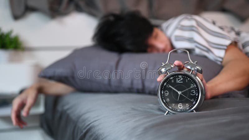 Hombre tirado en la cama y parando el despertador. imagen de archivo libre de regalías
