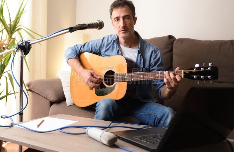 Hombre tocando guitarra con micrófono y laptop en sofá imagenes de archivo