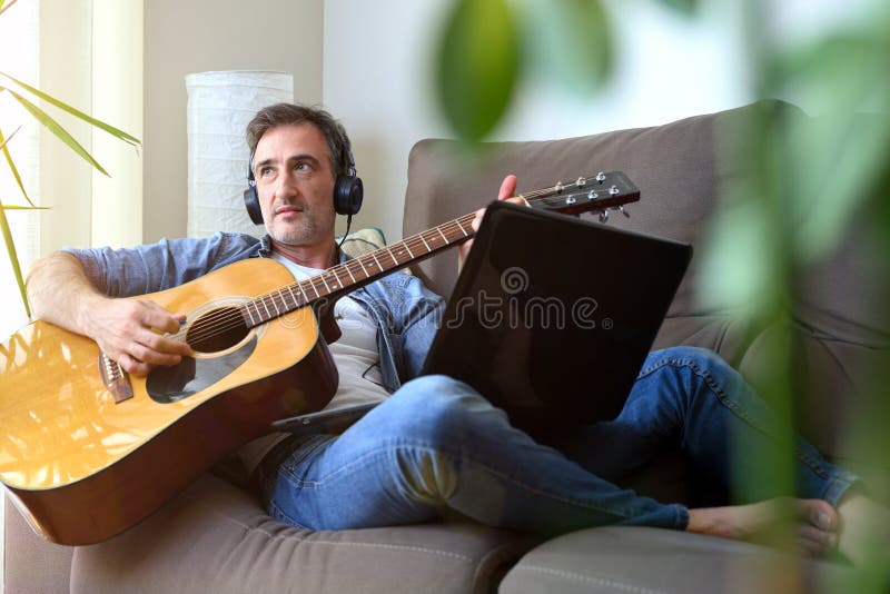 Hombre tocando guitarra y escuchando desde una laptop en casa imagen de archivo libre de regalías