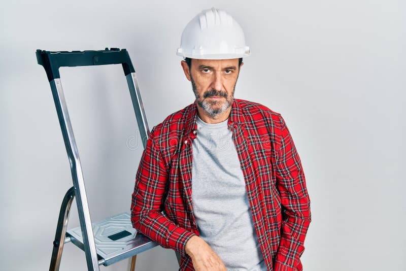 Hombre trabajador hispano de mediana edad usando actitud de pensamiento escalera y expresión sobria luciendo seguro de sí mismo fotografía de archivo