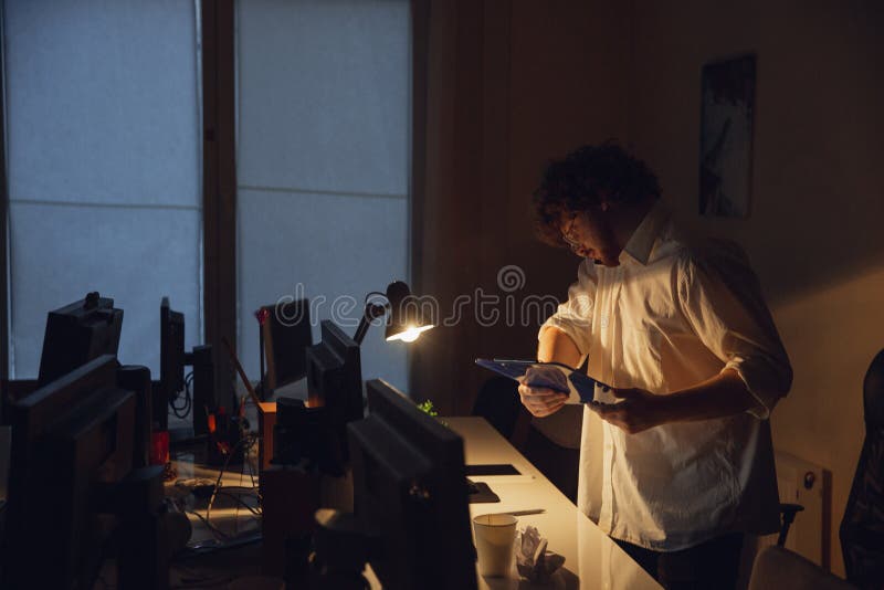 Hombre trabajando solo en el cargo durante la cuarentena del coronavirus o del COVID-19, permaneciendo hasta tarde en la noche foto de archivo libre de regalías Hombre trabajando solo en el cargo durante la cuarentena del coronavirus o del COVID-19, permaneciendo hasta tarde en la noche foto de archivo libre de regalías