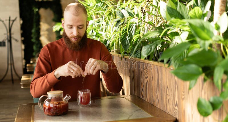 Hombre vertiendo azúcar de un palo en una taza de té sentado en un café verde interior en un día soleado fotografía de archivo libre de regalías
