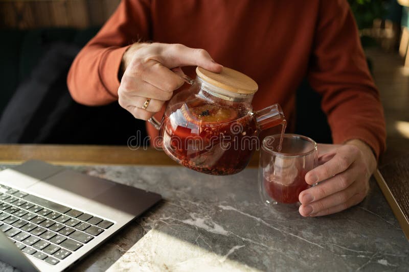 Hombre vertiendo té de fruta mientras trabaja en una laptop imagen de archivo libre de regalías