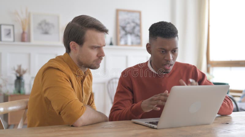 Hombre y joven africano reaccionando a la pérdida en laptop imagen de archivo libre de regalías