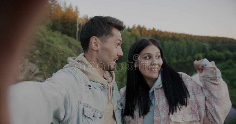 Hombre y mujer alegre pareja hablando apuntando a río y bosque haciendo videollamadas en línea en las montañas