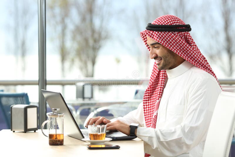 Hombre árabe del saudí que trabaja en línea con un ordenador portátil fotografía de archivo libre de regalías