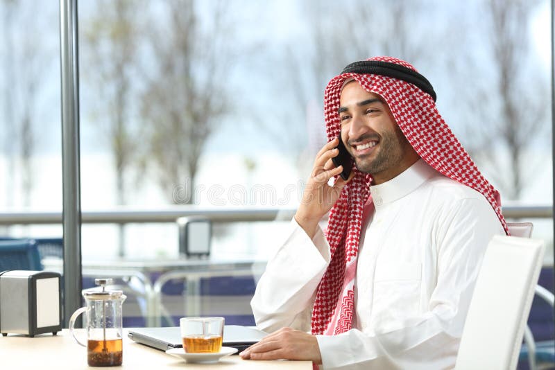 Hombre árabe feliz que habla en el teléfono en una cafetería imagen de archivo libre de regalías