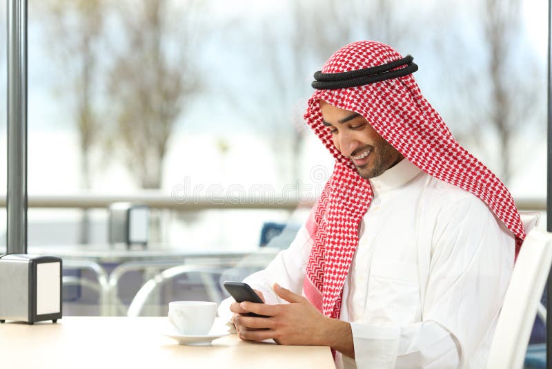 Hombre árabe feliz usando un teléfono elegante en una cafetería fotografía de archivo