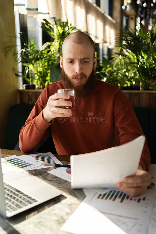 Hombres caucásicos barbudos y guisantes llevan pullover naranja trabajando en un moderno informe de lectura de cafés y tomando té fotografía de archivo libre de regalías