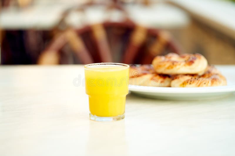 Home-baked pastries sprinkled with sesame seeds on a white plate with a glass of freshly squeezed organic orange juice