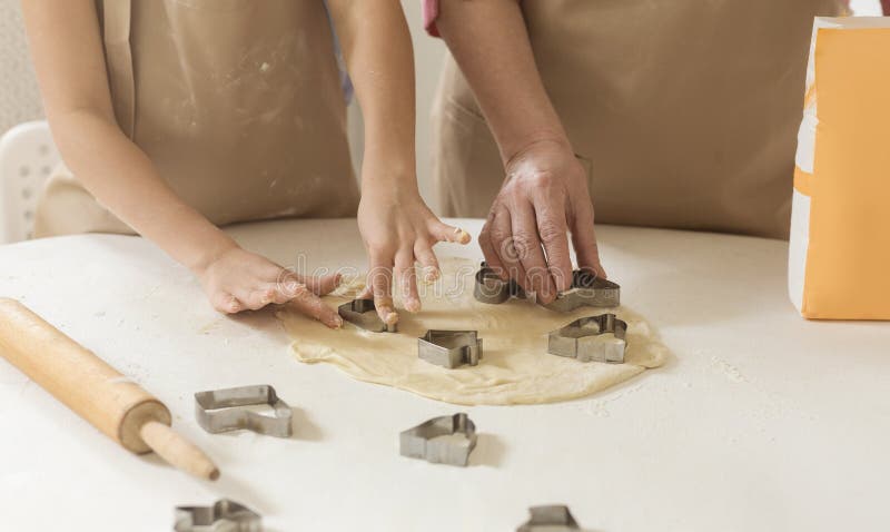 Home baking. Child and granny cutting cookies out of raw dough at table, closeup