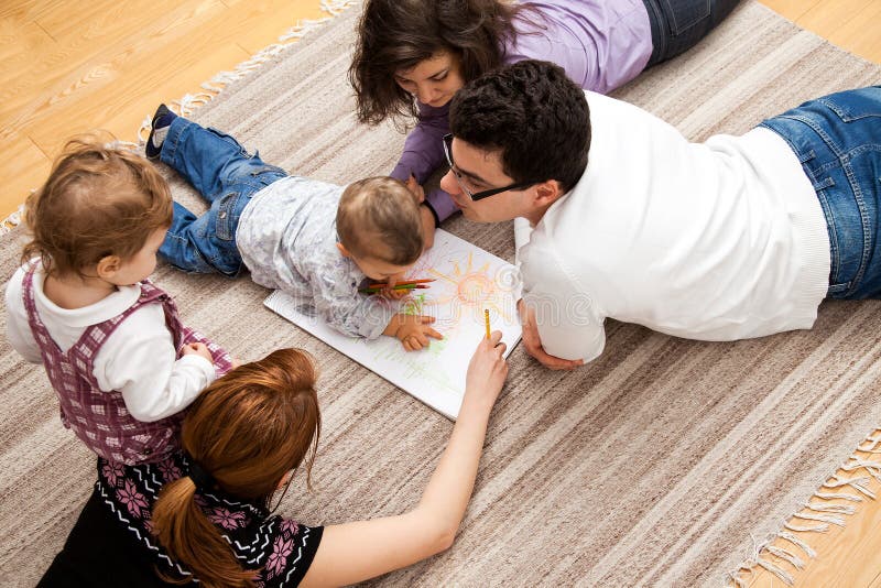 Family group of five - two babies and three adults lying on the carpet, drawing a picture together. Family group of five - two babies and three adults lying on the carpet, drawing a picture together.